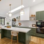 Zielona kuchnia z wyspą w minimalistycznym wnętrzu z drewnianą podłogą